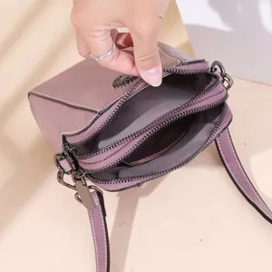 Detailed view of a purple leather crossbody phone bag with multi zipper compartments and strap.