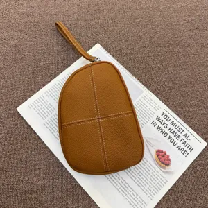 Detail shot of a premium Togo genuine leather wrist pouch in caramel brown with contrast stitching.