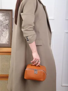 Detail shot of a brown leather cosmetic bag featuring a secure double zipper and top handle.