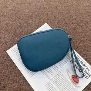 Detail view of blue textured genuine leather wrist pouch with zipper and strap on newspaper.