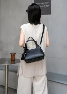 Black genuine leather shoulder crossbody bag for women with chic pendant and top handle, detail view.