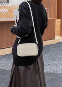Detail shot of the beige leather shoulder bag worn crossbody, showcasing fine texture and hardware.