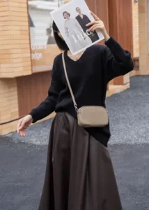 Detailed view of a stylish khaki leather crossbody bag worn with a black sweater and skirt.