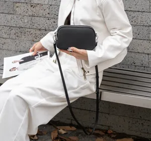 Close-up detail of black leather crossbody bag worn by model, showing texture and dual zippers.