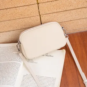 Minimalist beige genuine leather crossbody camera bag with metal zipper and fine strap.