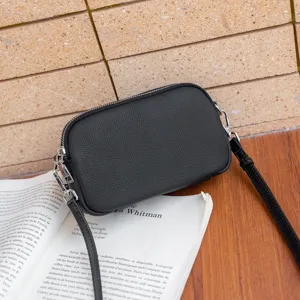 Black genuine leather cross-body bag, pebble grain texture, compact design with zipper.