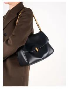 Black leather shoulder bag detail showing the gold chain strap and metal lock closure.