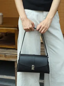Detailed view of the black leather shoulder bag, showcasing metallic lock and strap design.