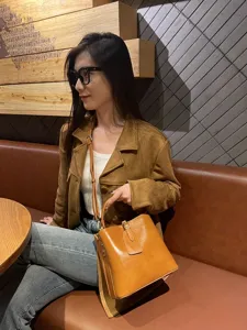 Detail shot of the retro vegetable tanned leather bucket bag worn by model in cafe setting.