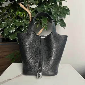 Primo piano dettagliato di borsa a secchiello nera in pelle con lucchetto e manici argentati.