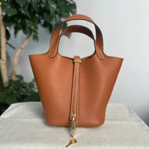 Dettaglio di una borsa a secchiello in pelle marrone con cuciture e lucchetto in metallo.