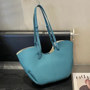 Dettaglio borsa tote in pelle blu con design ad ali, texture martellata e doppia tracolla.