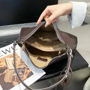 Dettaglio borsa a spalla hobo in pelle marrone con ampi scomparti interni e tasche con zip.