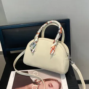 Detalle de bolso bowling de cuero blanco crema con asa de pañuelo de seda y correa cruzada.