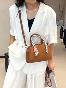 Elegante bolso de bolos de cuero marrón con asa superior y correa, pañuelo chic.
