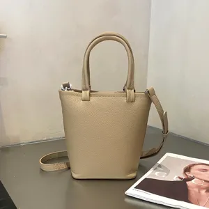 Minimalistische beigefarbene Leder-Eimer Tasche mit Henkel und Schultergurt für Damen.