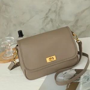 Detail shot of taupe leather crossbody bag featuring metal turn-lock closure and adjustable strap.