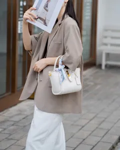 Close-up detail of white leather handbag featuring elegant metal lock and chic silk scarf decor.