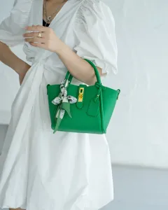 Green leather handbag detail showcasing gold hardware, elegant turn-lock and silk scarf.