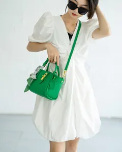 Detail shot of a vibrant green leather handbag with gold hardware and chic silk scarf accent.