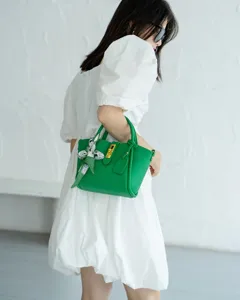 Detail shot of green leather handbag with gold lock and chic printed twilly scarf.