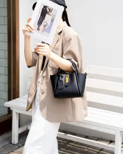 Close-up of black leather bucket handbag with metal lock and handles in lifestyle scene.