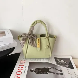 Green leather bucket bag detail featuring luxury metal turn-lock and stylish scarf accent.