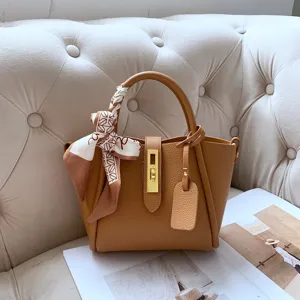 Brown leather bucket bag with top handle, elegant gold lock and stylish scarf accessory.