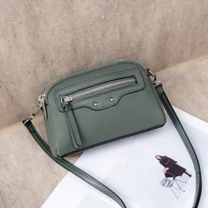 Dark green leather crossbody bag detail view, showing front zipper pocket and metal studs.