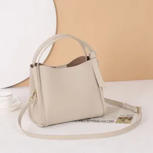 Detail view of a stylish beige leather bucket bag with dual handles and crossbody strap.