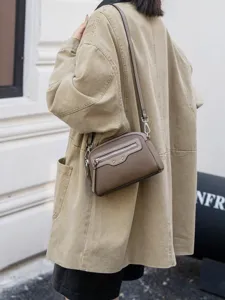 Detailed shot of a stylish brown leather crossbody bag with front zipper and metal studs.
