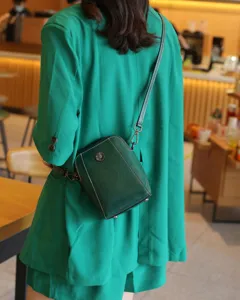 Sac bandoulière en cuir vert pour femme, finition cire avec fleur en métal et coutures blanches.