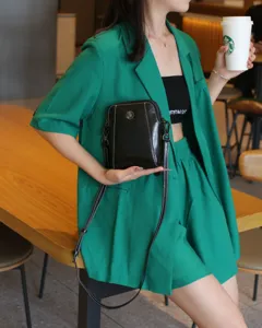 Sac bandoulière en cuir noir détaillé avec des surpiqûres blanches et pendentif.