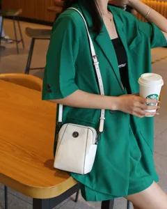 Vue détaillée du sac bandoulière en cuir blanc, pochette de téléphone compacte avec bouton en métal fin.