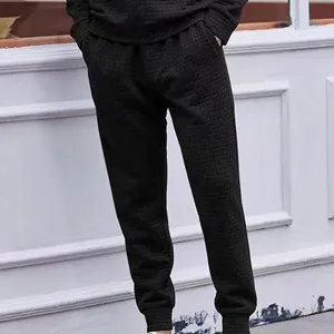 Detail view of black textured jacquard knit sweatpants with elastic cuffs and drawstring.