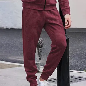 Detailed shot of men's burgundy waffle knit sweatpants featuring textured grid fabric and ribbed cuffs.