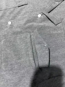 Close-up detail of men's grey short-sleeve linen shirt showing pocket and white button.
