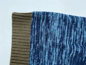 Close-up detail of mens knit sweater cuff, ribbed brown sleeve and blue heathered knit.