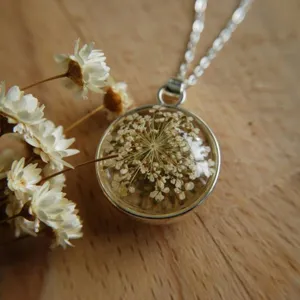 Close-up detail of a round glass pendant featuring a delicate white dried flower on wood.