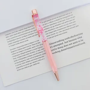 Detail of a pink ballpoint pen with dried flowers floating in oil atop an open book page.
