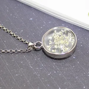 Close-up of a silver necklace featuring a round glass ball with a real dried flower inside.