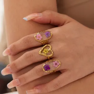 Close-up detail of gold heart and oval rings featuring colorful dried flowers in resin.