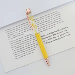 Detailed view of a yellow ballpoint pen with dried flowers floating in oil on a book