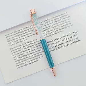 Close-up detail of a teal metal ballpoint pen with dried flowers in an oil-filled barrel