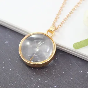 Close-up of dried dandelion seed inside a round glass pendant with a gold frame