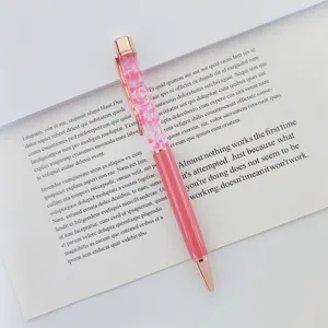 Close-up of elegant rose gold floating ballpoint pen with pink dried flowers and oil