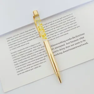 Detail of gold metal ballpoint pen featuring yellow dried flowers in clear oil barrel