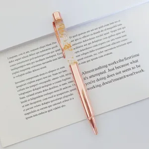 Elegant rose gold ballpoint pen with yellow dried flowers displayed on an open book.