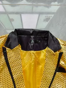 Détail de veste de costume à sequins brillants pour homme, avec revers noir et tissu doré élégant.
