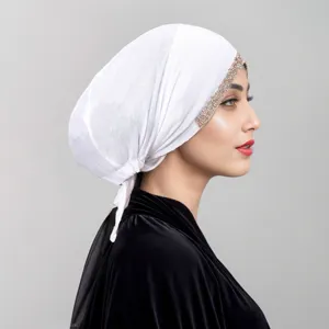 Detailansicht der weißen Turbanmütze mit glitzerndem Strassbesatz und Bindeband-Design.